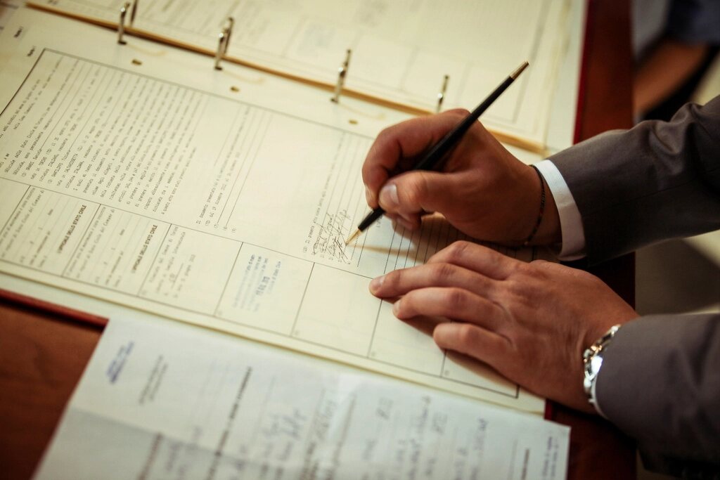 Mână care semnează un document pe un birou